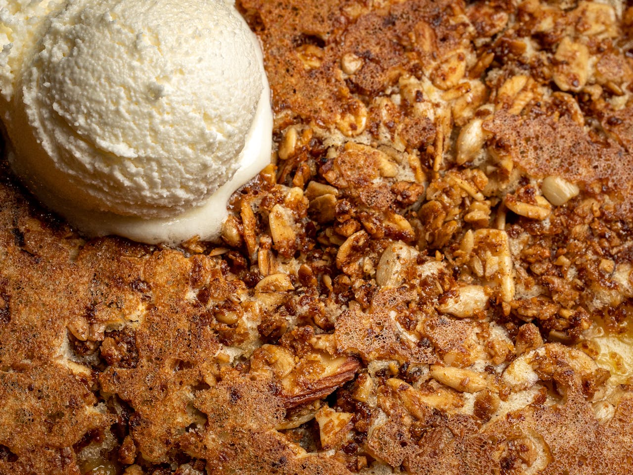 Close-up of crunchy almond cake topped with creamy vanilla ice cream.
