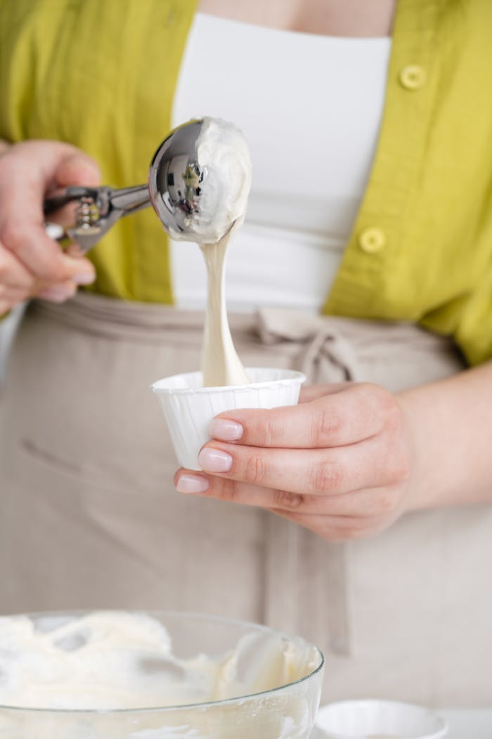 Close-up of a woman scooping creamy vanilla ice cream into a cup.